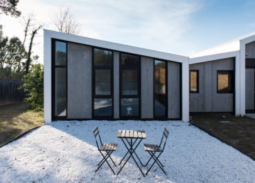 Terraza jardín exterior de una casa modular, con una mesa y dos sillas, día soleado